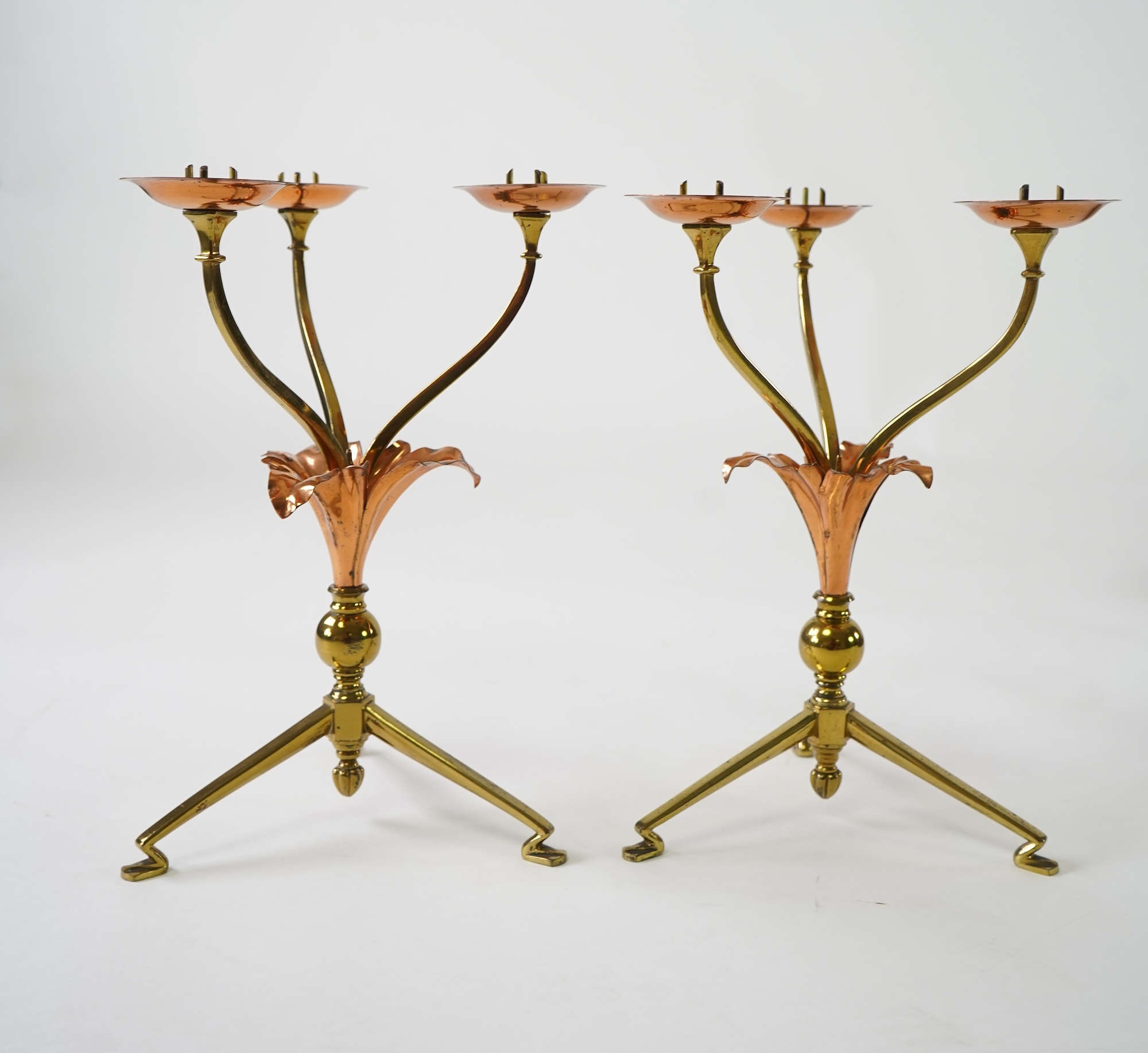 W.A.S. Benson & Co.: A pair of Arts and Crafts gilt brass and copper three branch candelabra